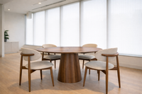 Table ronde en noyer massif design avec pied central dans un espace intérieur lumineux et épuré avec chaises en tissu beige