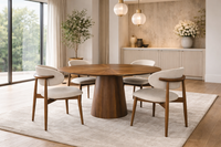 Table ronde en noyer massif design avec pied central dans une salle à manger élégante et lumineuse avec chaises en tissu beige